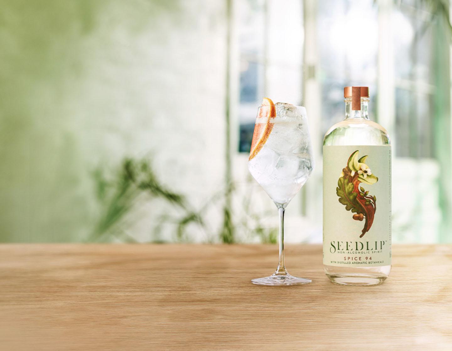 Bottle of Seedlip Spice 94 on table beside cocktail