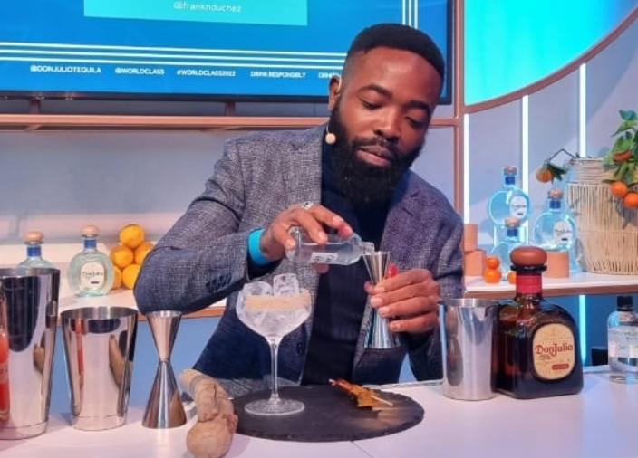 Francis Ndungu vertiendo una pequeña botella de líquido transparente en una medida junto a un vaso con hielo