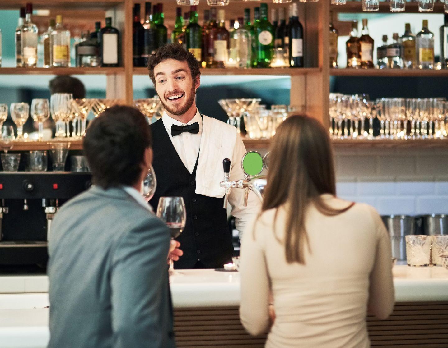 Barkeeper steht hinter der Bar und unterhält sich mit zwei Gästen 