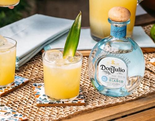 Botella de Don Julio Tequila Blanco junto a un cóctel aderezado con una hoja.