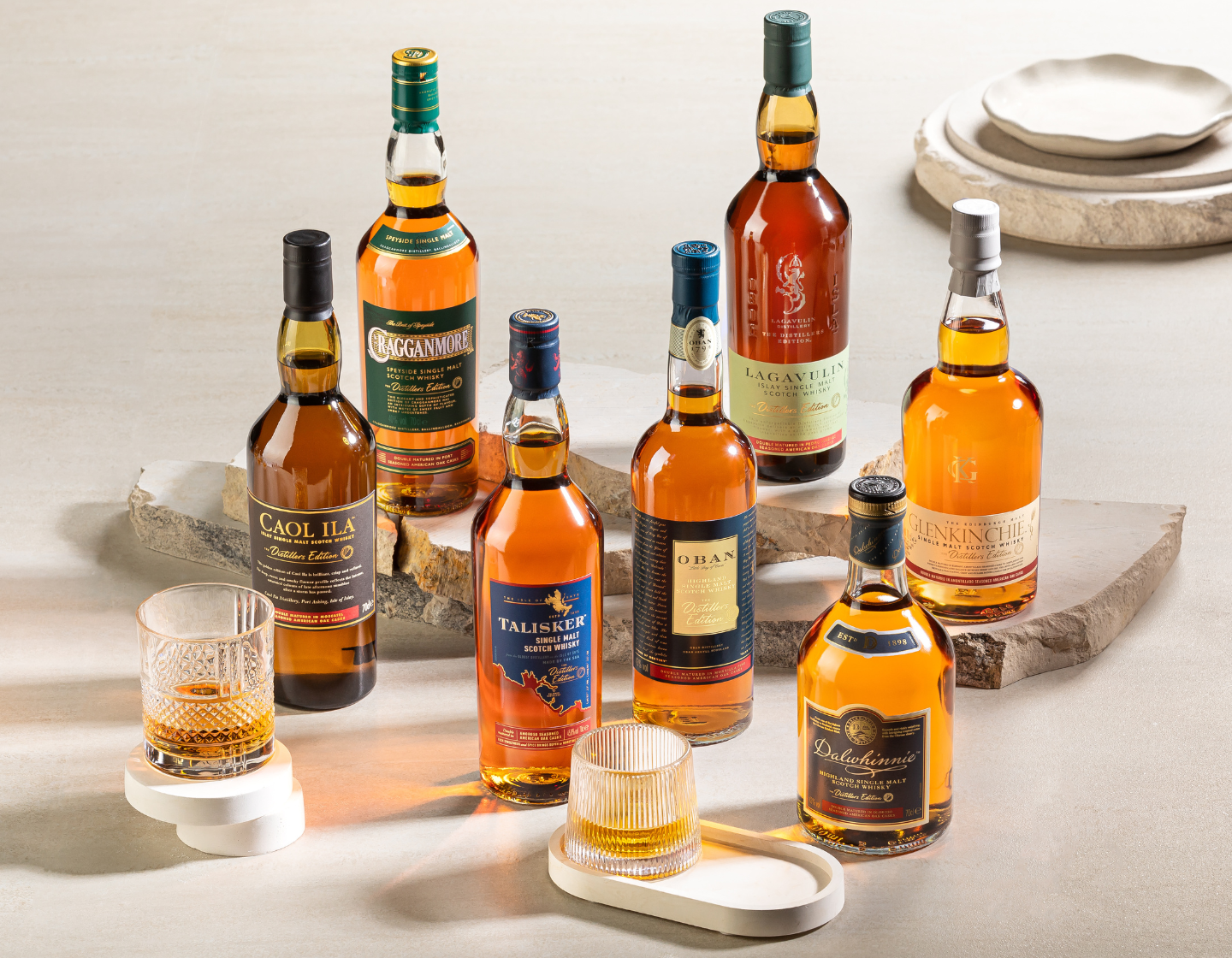 Colección de siete botellas diferentes de whisky de malta contra una mesa de piedra gris 