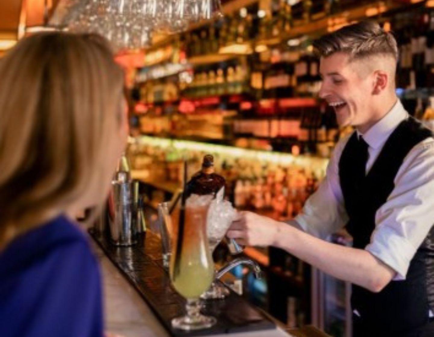 Bartender serves customer a yellow cocktail