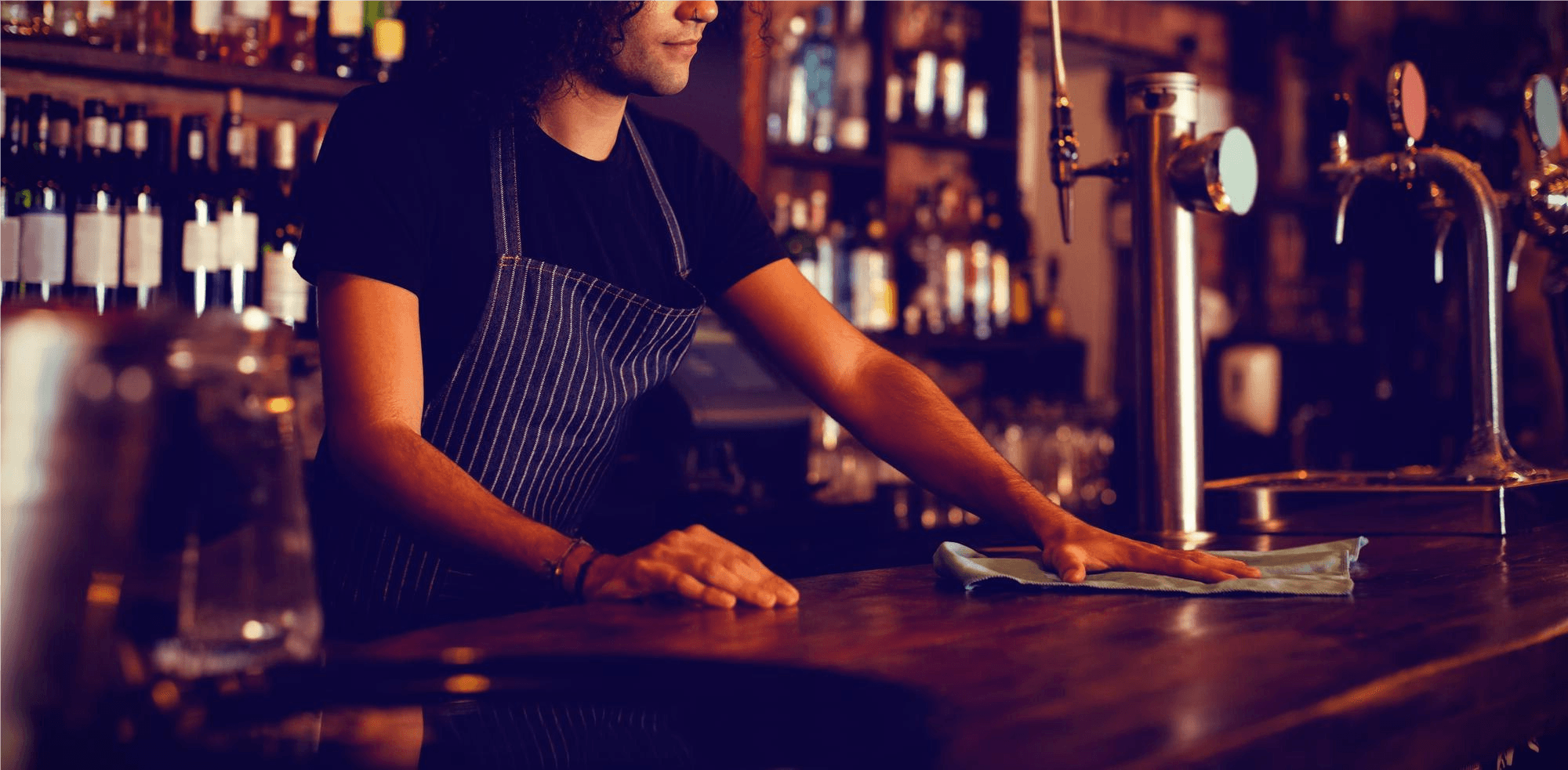 Personal del bar trabajando detrás de una barra ocupada con clientes sentados en la barra con comida y bebidas. 