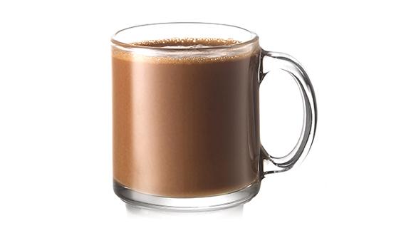 Uma bebida Talisker Campfire Hot Chocolate, ao lado de uma garrafa de uísque Talisker, em uma mesa em frente a uma poltrona e fogueira alta. 