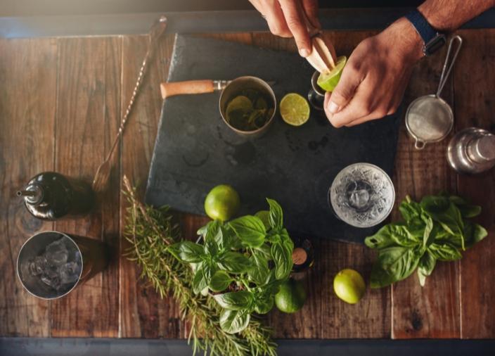 Vista aérea de la barra con hierbas, herramientas de bar y limones.