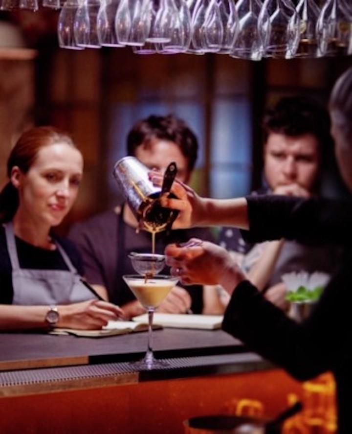 Drei Personen schauen zu, wie ein Drink gemixt wird