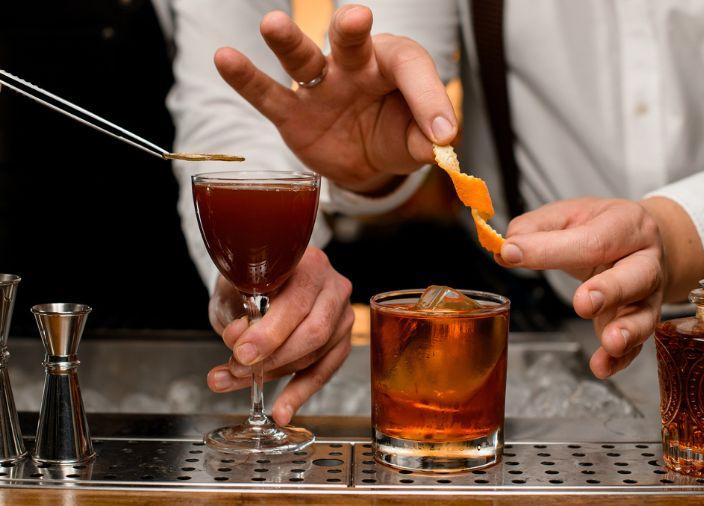 Two bartenders garnishing cocktails with orange slices for current bar indsutry trends.