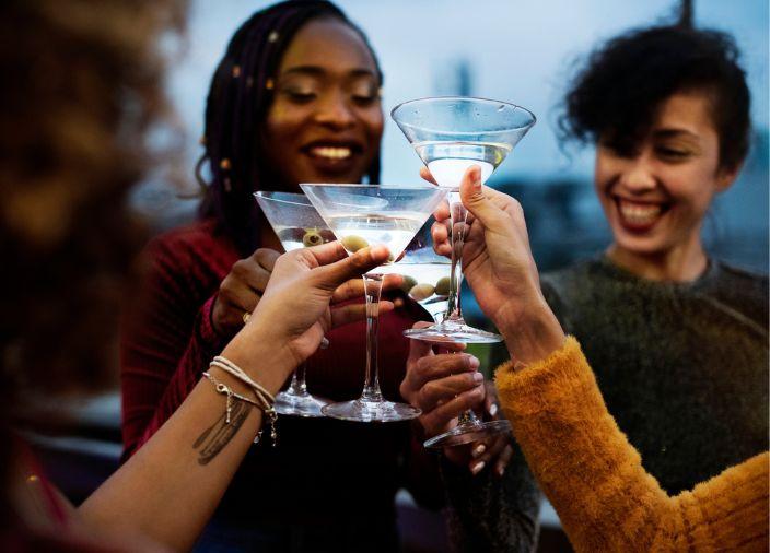 Four friends smiling and clinking four martini cocktails together.