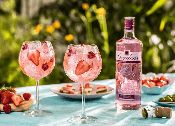 Botella de ginebra Gordon’s Premium Pink junto a dos copas de gin-tonic sobre un fondo rosa y azul 