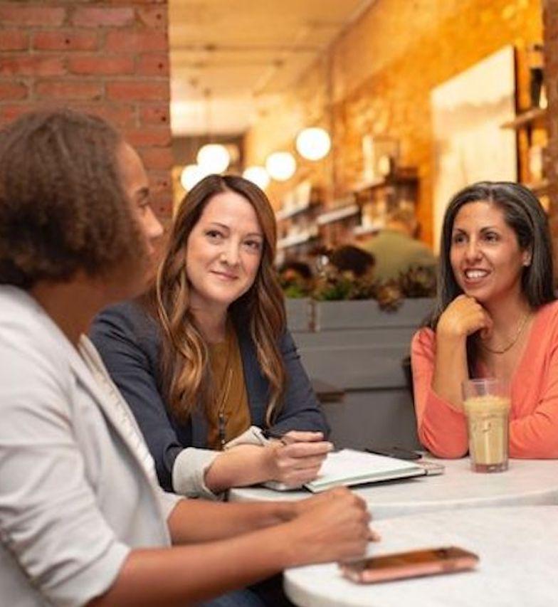 3 Personen sitzen an einem Tisch mit Stift und Papier und unterhalten sich