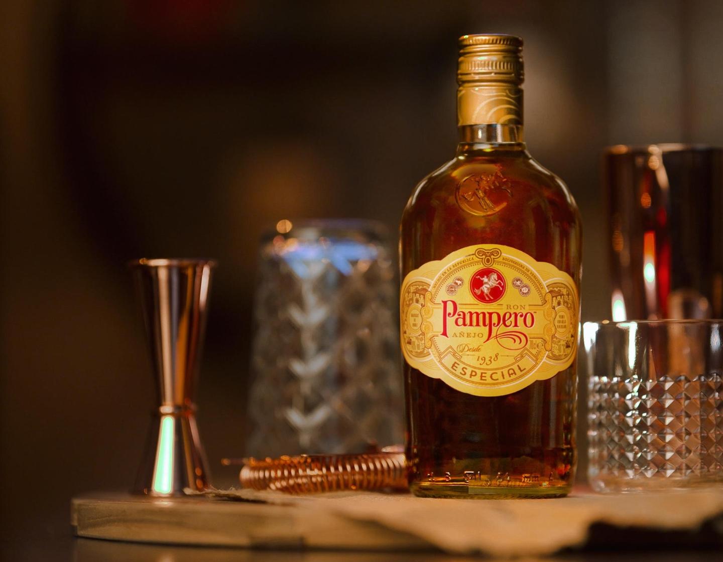 Bottle of Pampero Especial rum beside jigger with two cocktails in the background 