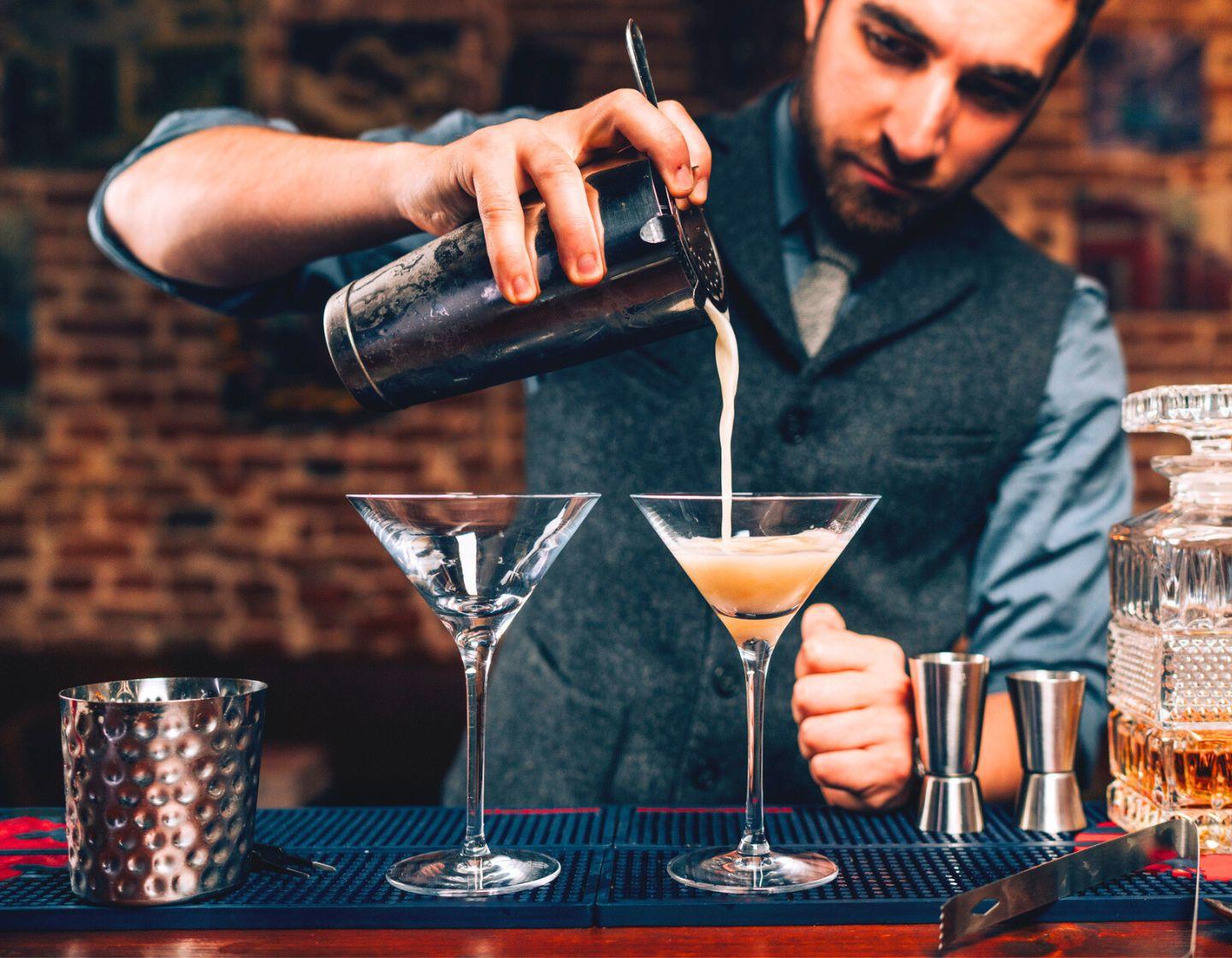Bartender pouring a cocktail from a shaker into a cocktail glass.