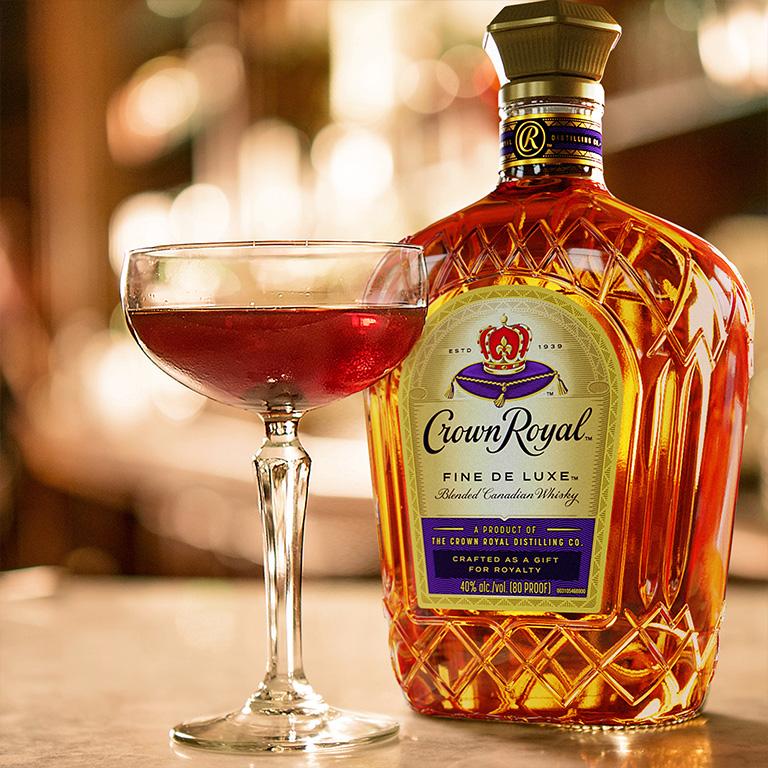 Bottle of Crown Royal whisky on table beside cocktail in coupe glass 