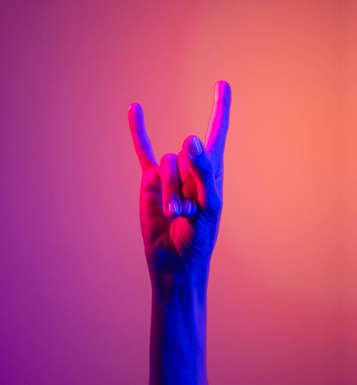 uma mão fazendo o símbolo do rock, conhecido como o "chifre" em um fundo gradiente