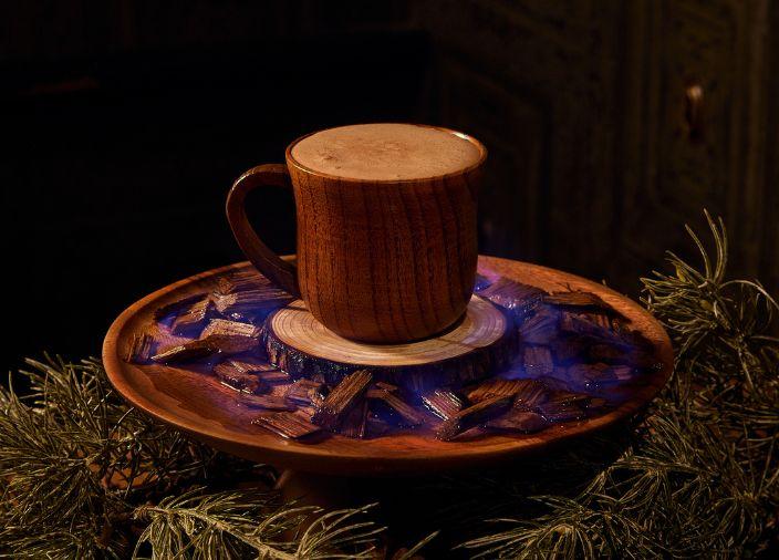 Un cóctel de chocolate caliente en una taza de madera y un plato rústico de madera.