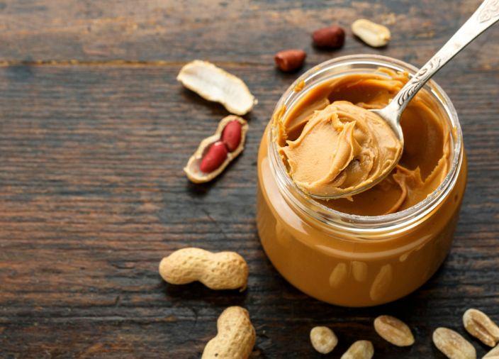 Peanut paste in an open jar and peanuts.