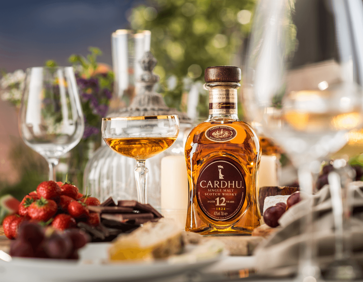 Bottle of Cardhu single malt whisky on table surrounded by plates of food and cocktail glasses 