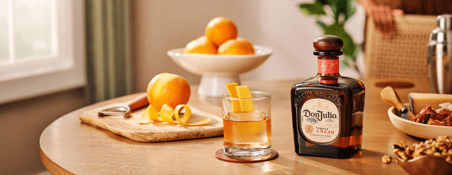 Bottle of Don Julio Añejo tequila and oranges standing in front of red door