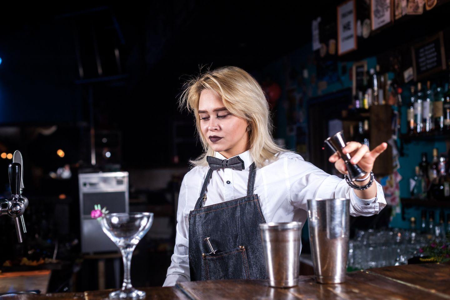 Imagem de uma bartender atrás do bar fazendo um coquetél