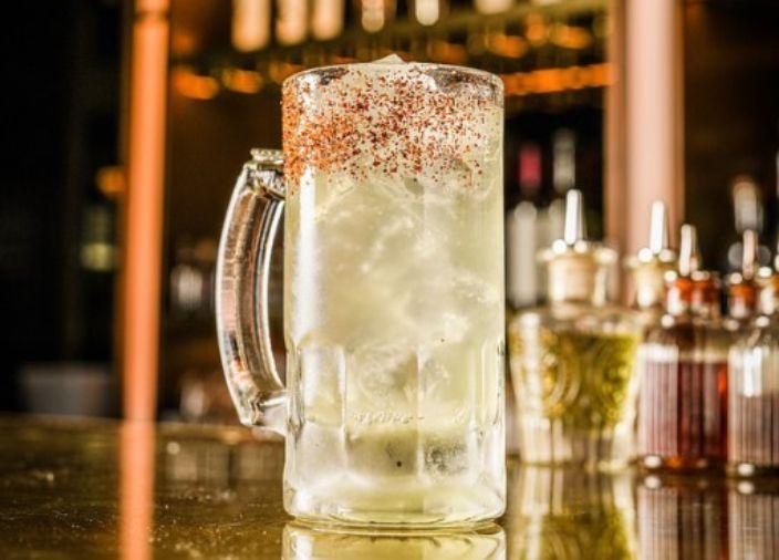 A yellow-tinted cocktail in a stein glass with a red, salted rim.