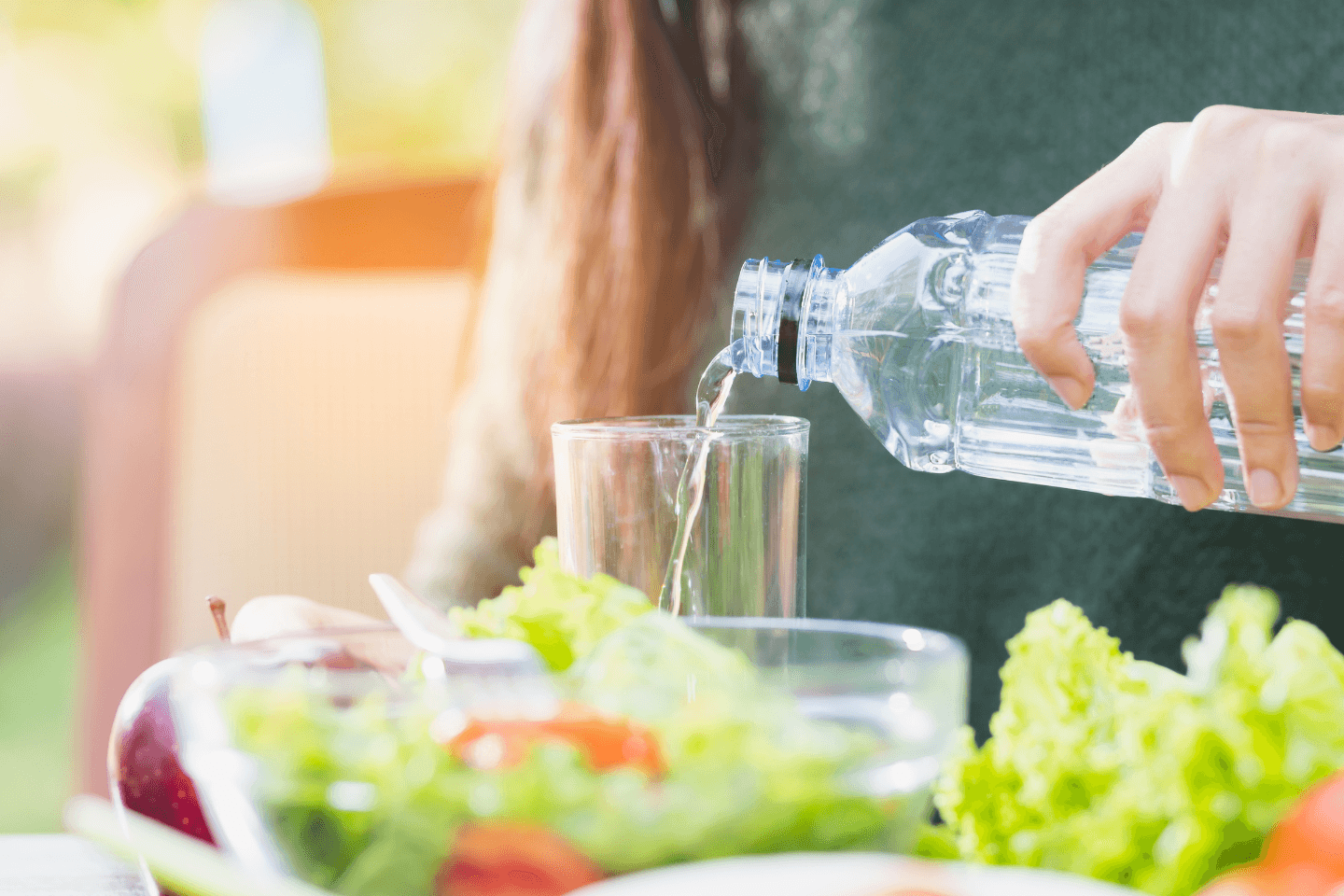 Agua sendo colocada em um copo e uma salada saudável ao lado