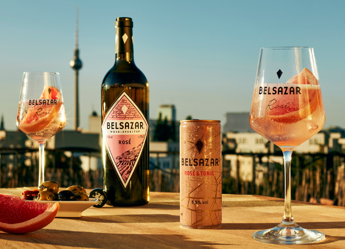 Bottle of Belsazar rosé outside on table at sunset beside two wine glasses filled with pink drinks  
