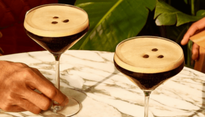 2 espresso martinis on a tsble with hands reaching