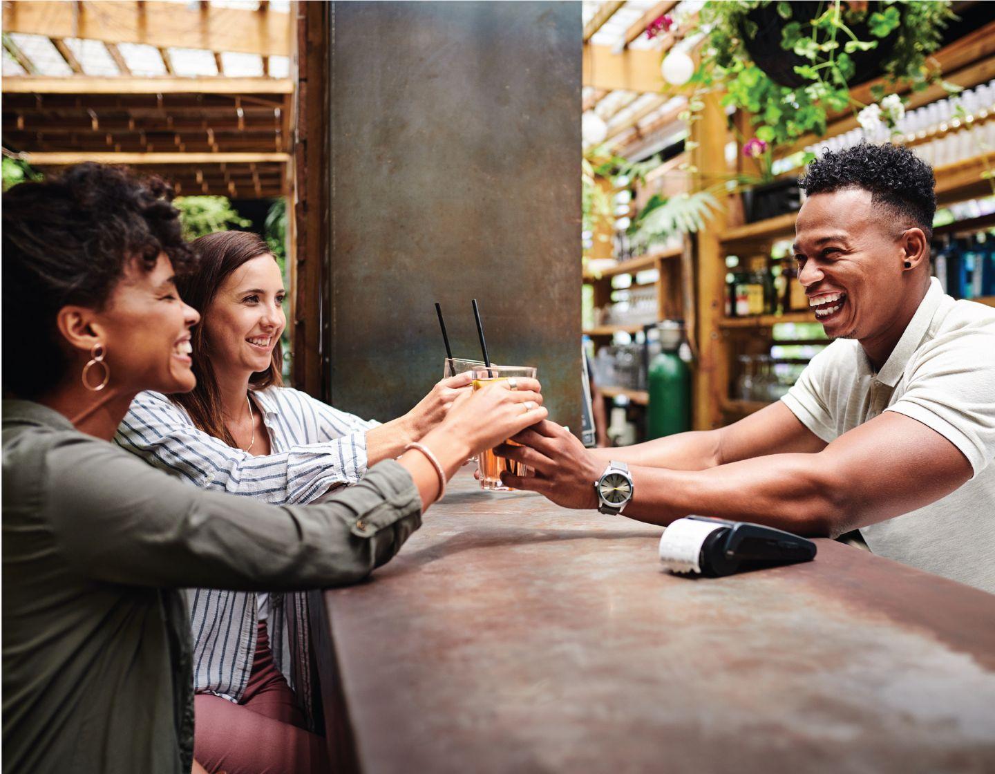 Smiling bartender serving cocktails to two happy customers.