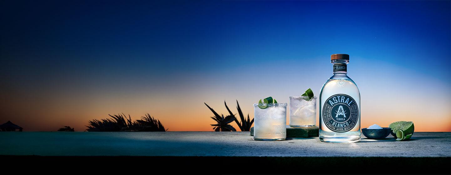 Bottle of Astral with two cocktails in front of landscape