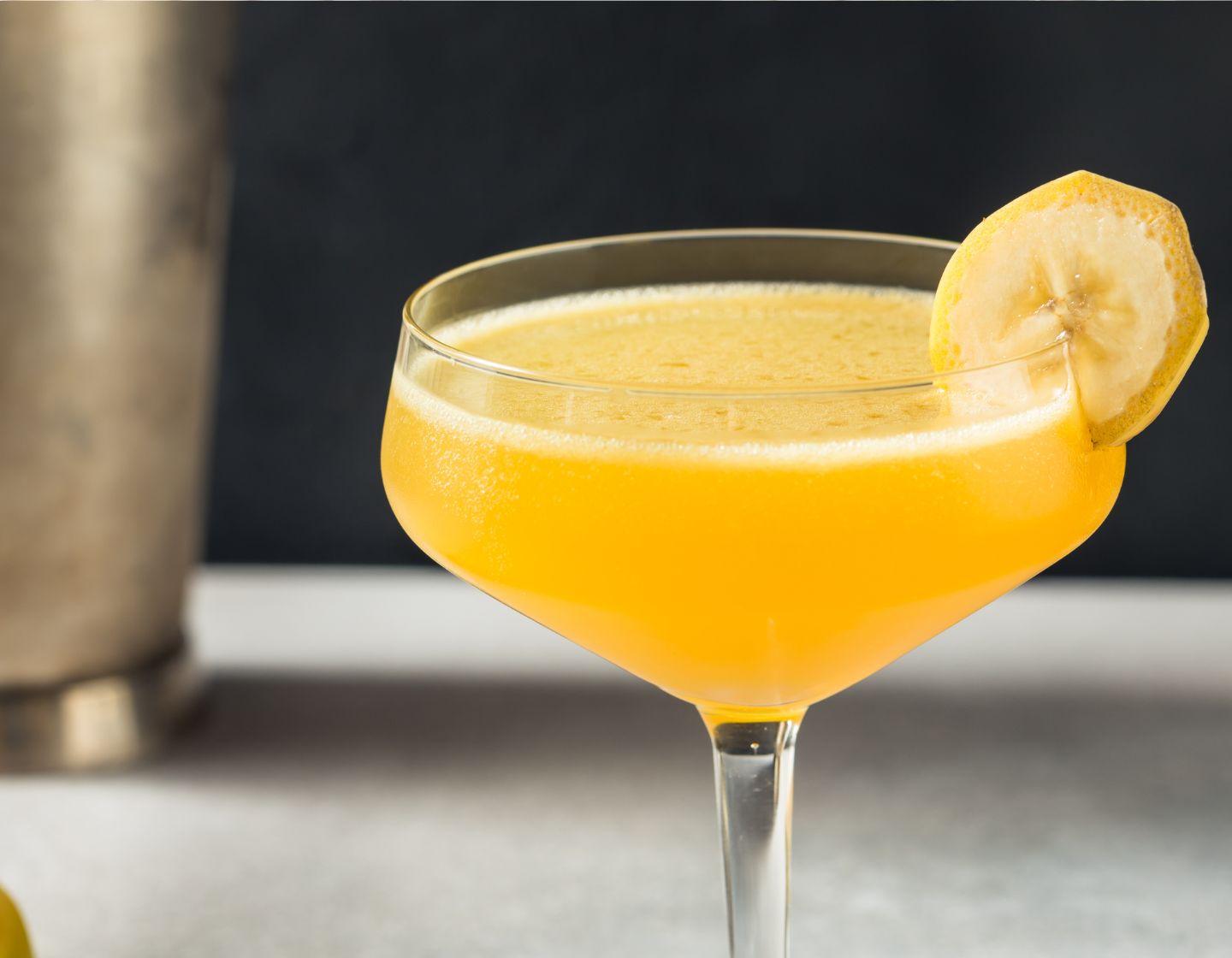 Yellow cocktail garnished with a banana slice.