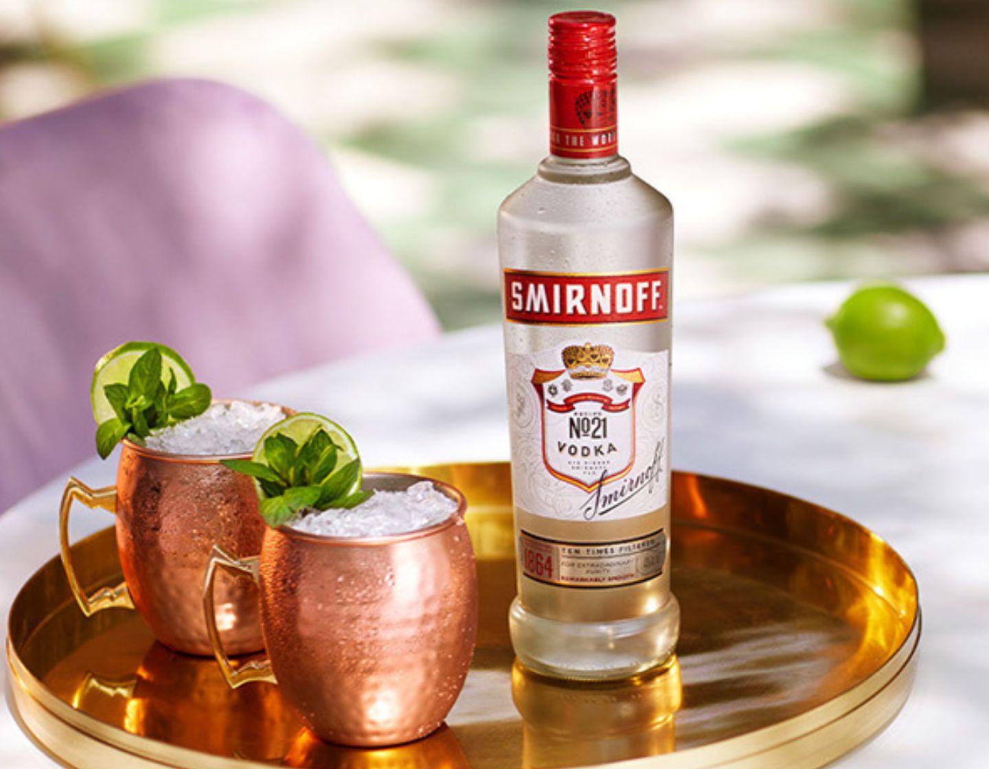 Smirnoff Vodka Bottle next to two vodka serves in brass cups 