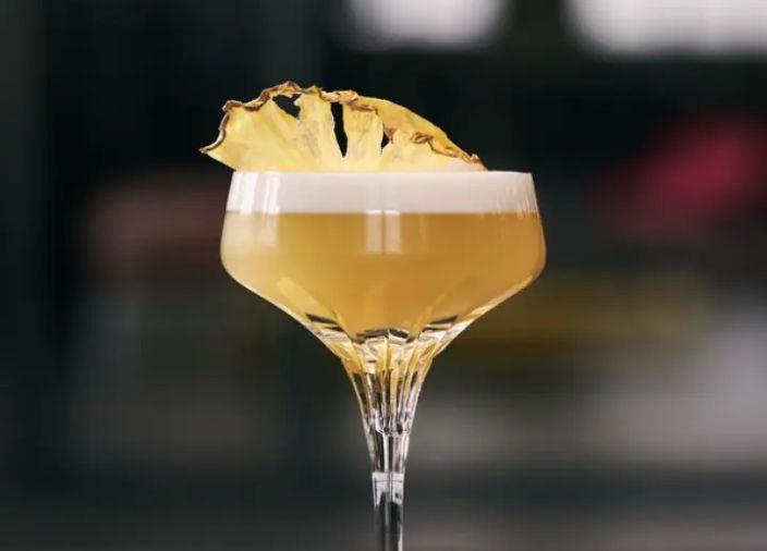 Cóctel agrio de vodka amarillo en una copa coupé con espuma y garnish de piña