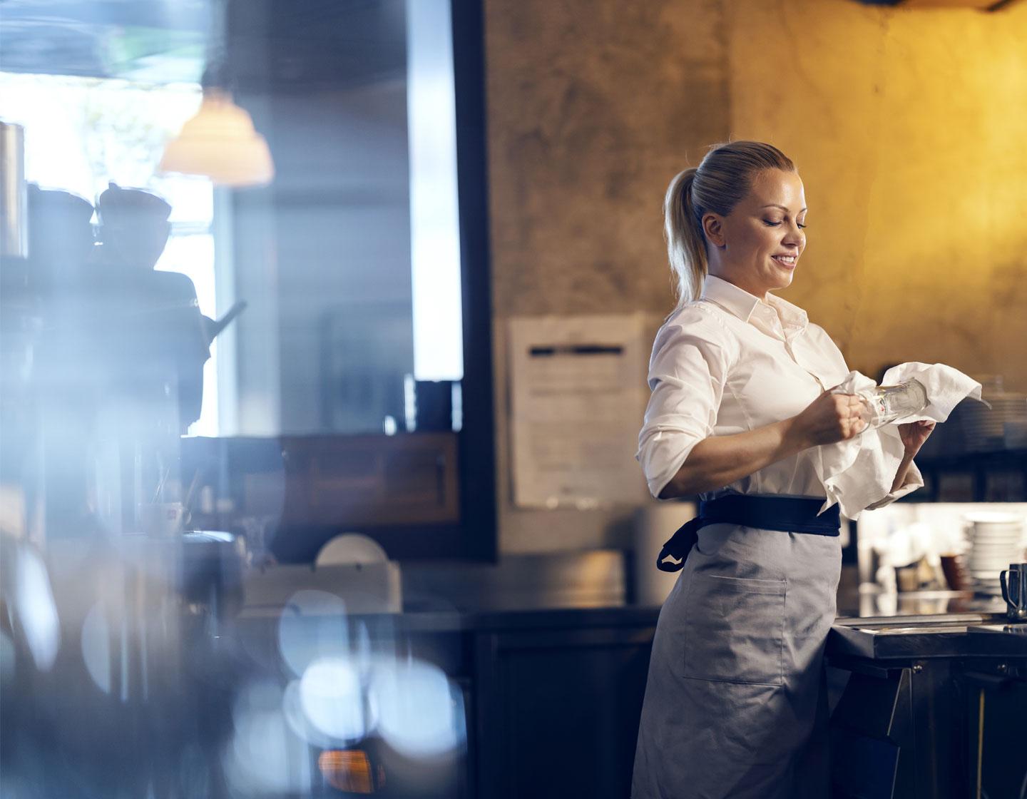 Female bartender behind bar drying a glass