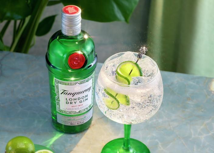 Bottle of Tanqueray London Dry Gin next to gin and tonic cocktail with lime garnish.