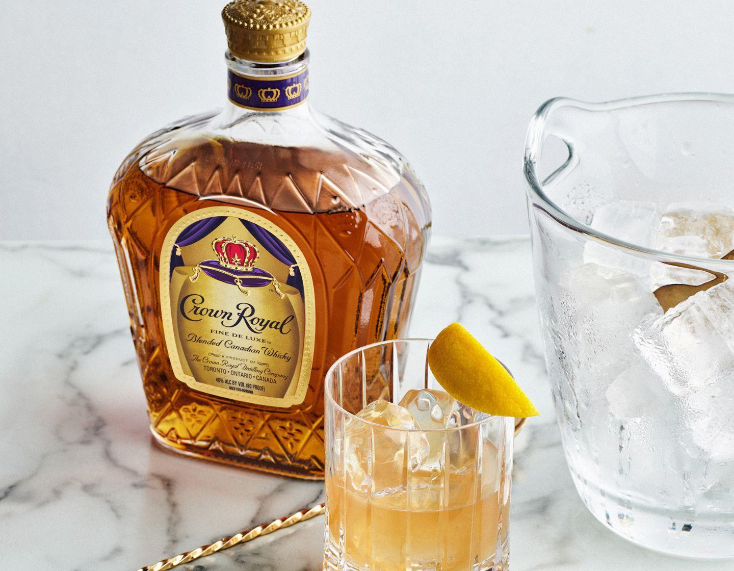 Bottle of Crown Royal whisky on table beside cocktail in coupe glass