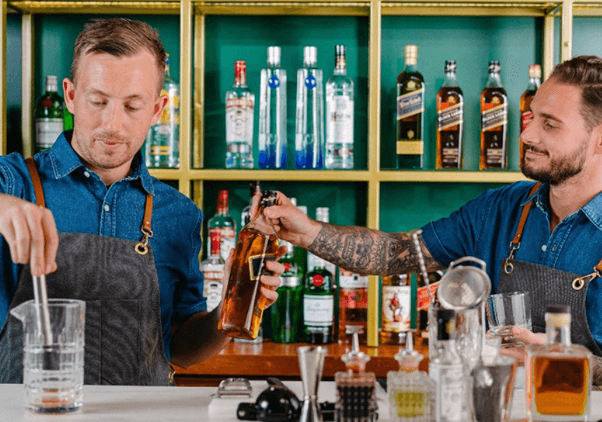 Dos bartenders detras de la barra preparando un cóctel 