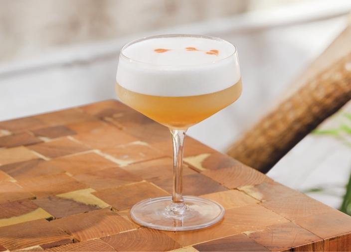 Cóctel agrio de vodka amarillo en una copa coupé con espuma y ganish de piña