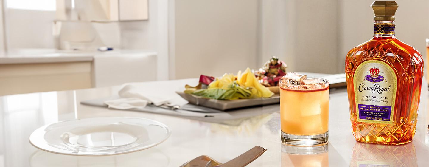 Bottle of Crown Royal whisky on table beside cocktail in coupe glass
