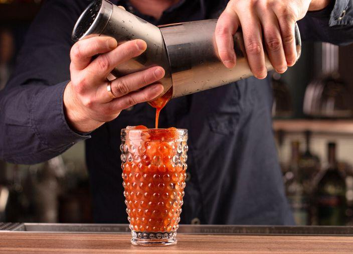 Red cocktail being poured into a glass.