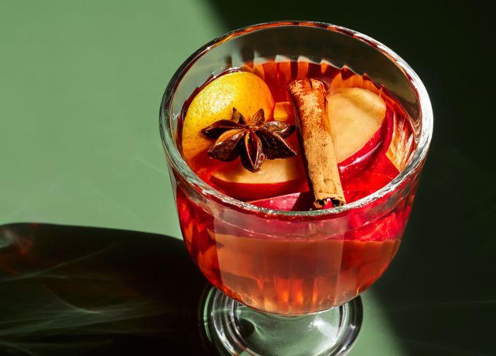 Ein roter Cocktail mit einer Zimtstange, geschnittenen Äpfeln und Nelken.
