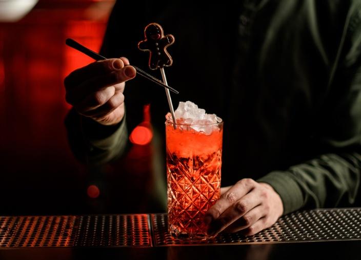 Un barman añadiendo un toque de jengibre como guarnición a un cóctel rojo con hielo