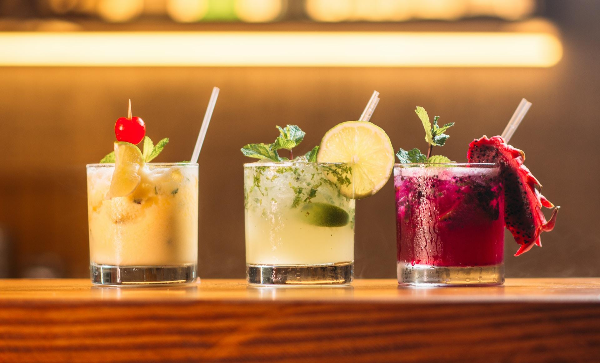 Drei Cocktails stehen mit Garnierung nebeneinander auf einem Holztisch