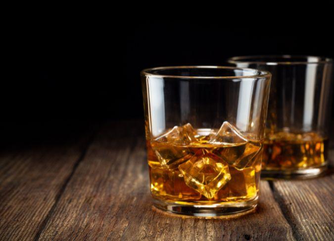  Bottle of Black & White whisky on wooden table surrounded by whisky tumblers