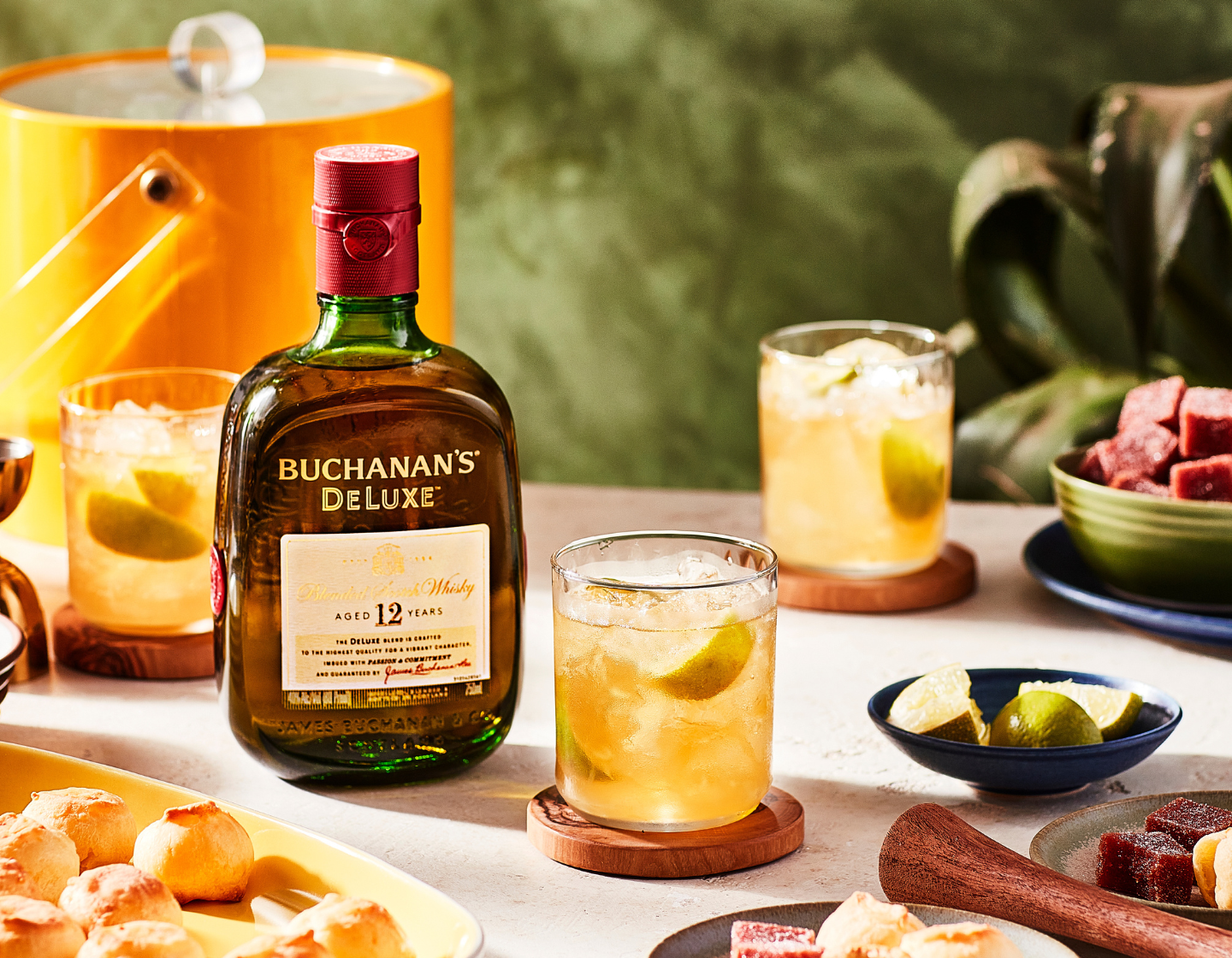 Garrafa de whisky Buchanan's Deluxe na mesa ao lado de comidas e bebidas variadas 