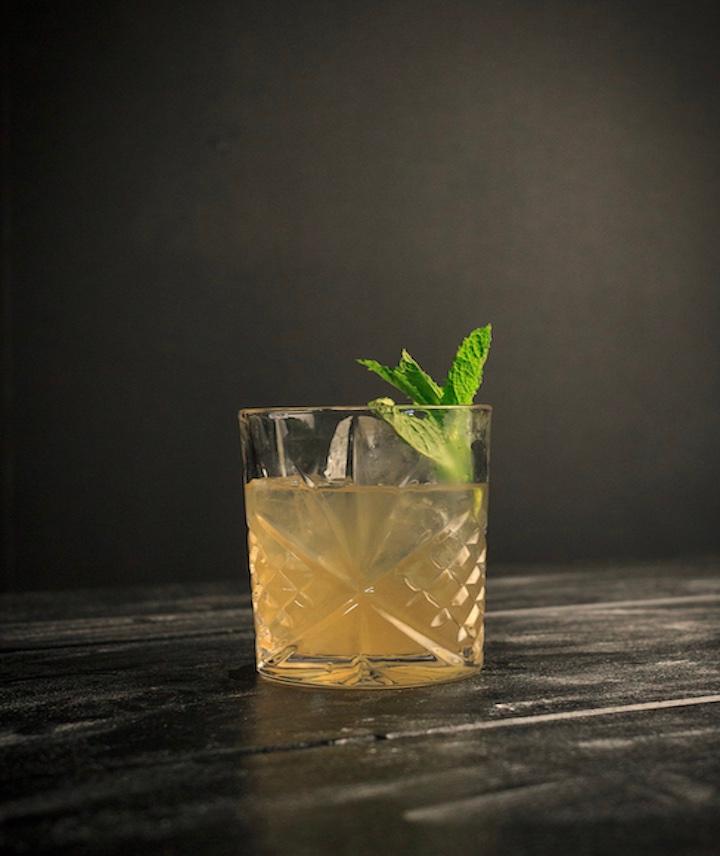 Ein gelber Drink mit Garnierung steht vor einem dunklen Hintergrund