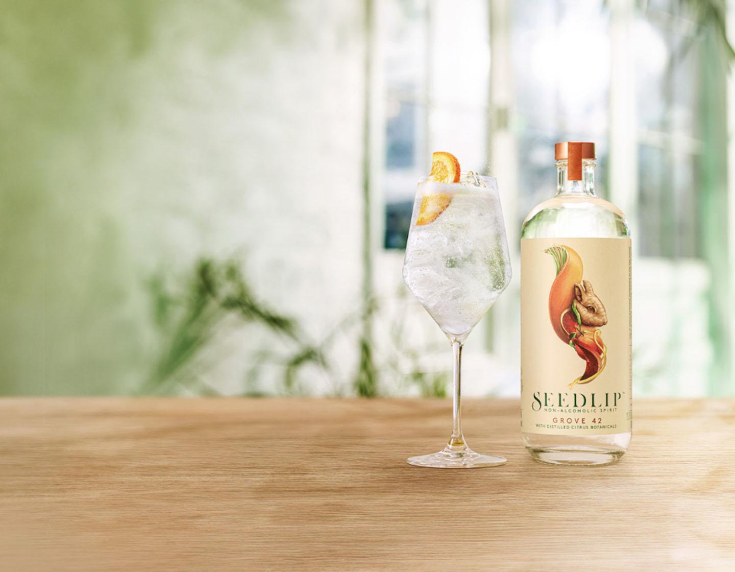 Bottle of Seedlip Grove 42 on table beside cocktail 