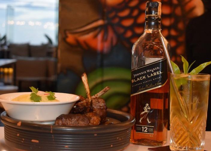 Eine Flasche Johnnie Walker Black Label steht neben einem orangegen Drink und einem Menü.