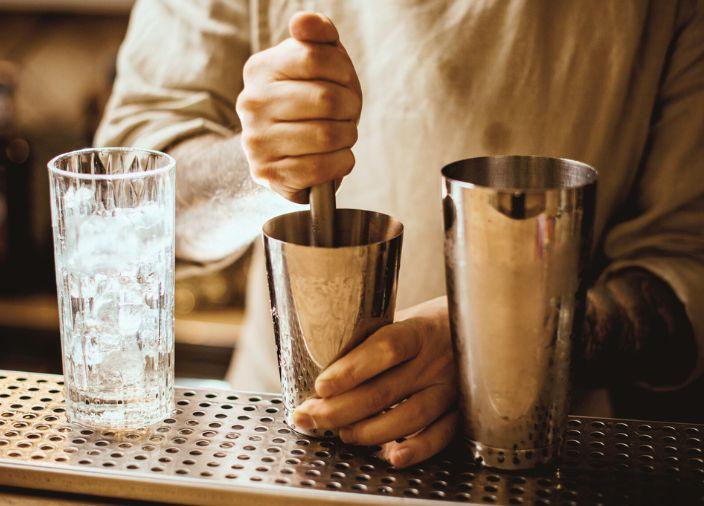 Bartender con mortero en una coctelera de acero.