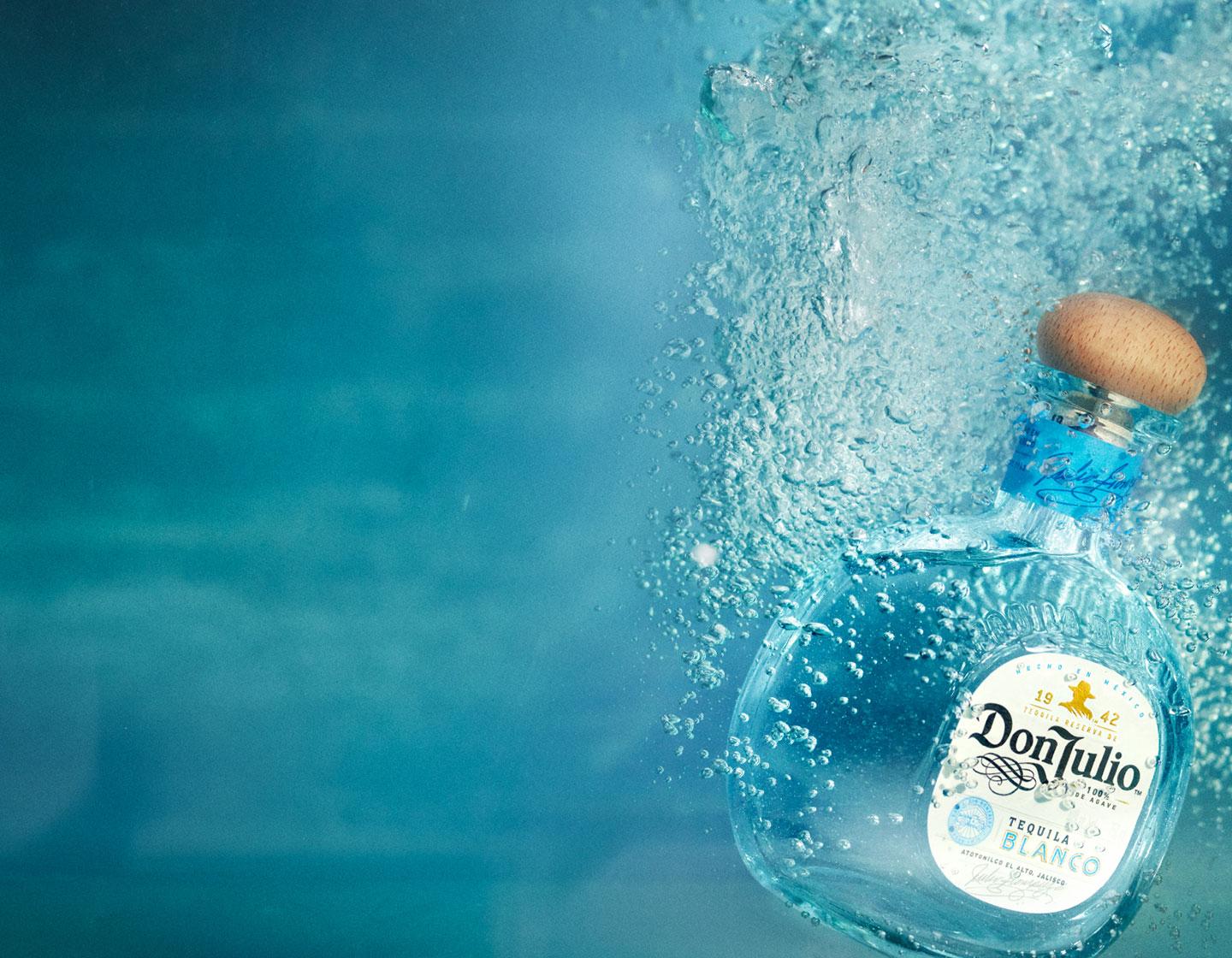 Botella de Don Julio Tequila Blanco junto a un cóctel aderezado con jalapeños y rodajas de lima. 