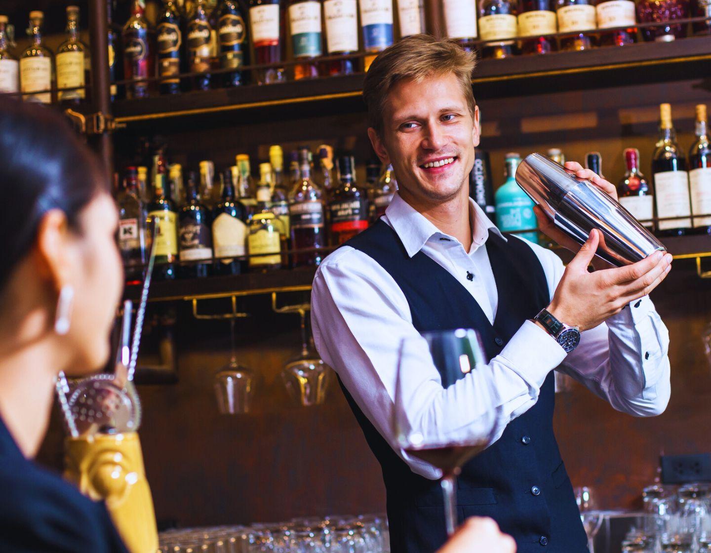 Barman servindo cliente em um bar segurando uma coqueteleira.